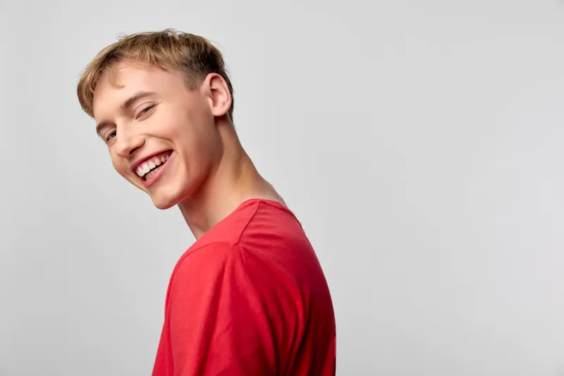Smiling male in a red shirt, turned slightly away from the camera, exuding casual happiness and a cheerful, approachable vibe for lifestyle, fashion, and marketing visuals