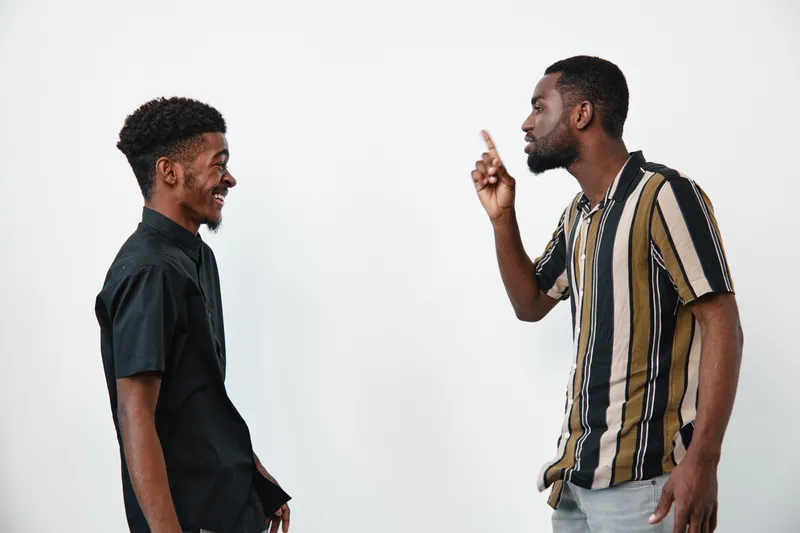 Two black men with dark skin having a conversation and smiling on white background. Casual clothing, communication, friendship, interaction, and positive mood between African ethnicity.