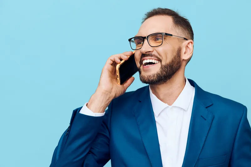 A confident professional man in a blue suit speaks on a mobile phone against an isolated colored background, conveying success, focus, and dynamic business emotion.