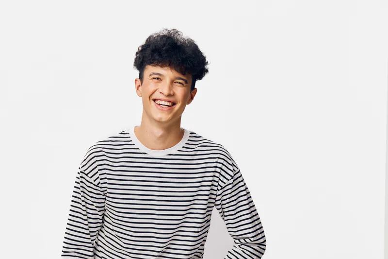 smiling man in striped shirt laughing while standing on white background, cheerful young male, casual clothing, happy expression, isolated studio portrait
