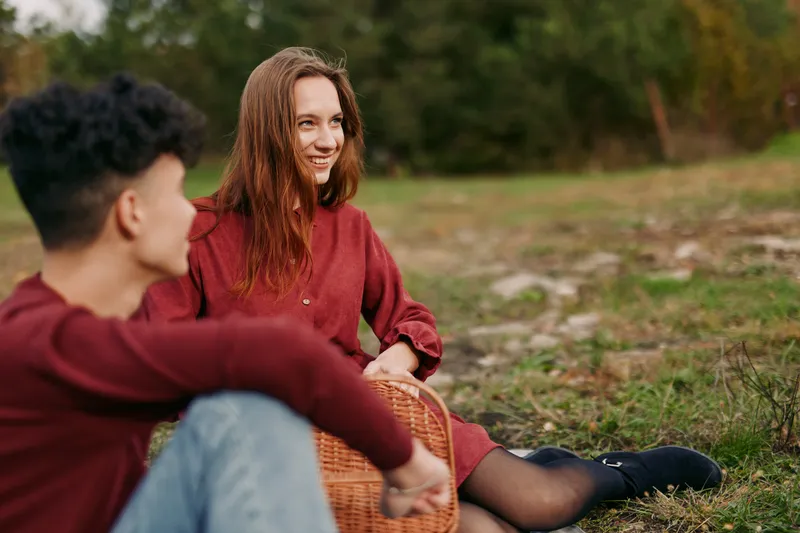 A candid outdoor moment shows authenticity and credibility as two friends sit on grass, sharing warm conversation under soft daylight, creating a genuine, relaxed connection.
