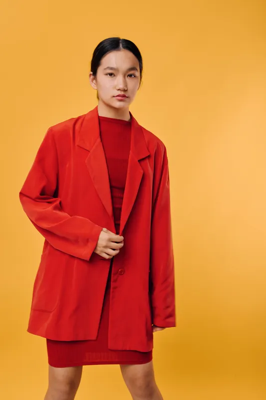 Young woman wearing red blazer and dress standing against yellow background with serious expression, fashion style and casual outfit for modern look and confidence.