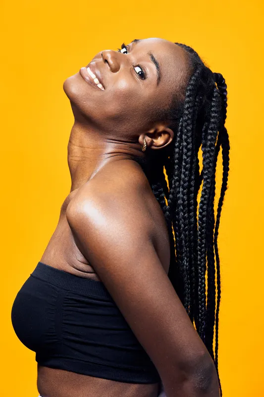 A joyful young woman with braided hair smiles brightly against a vibrant yellow background, exuding confidence and summer vibes perfect for fashion and lifestyle concepts