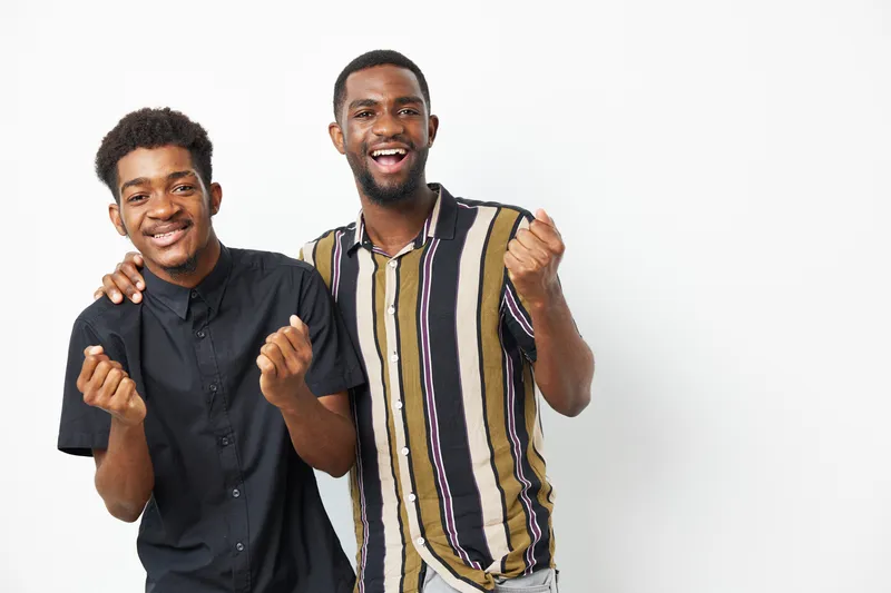 Two joyful black men celebrating together, showcasing happiness, friendship, and positive energy in a bright, light environment that uplifts the mood.
