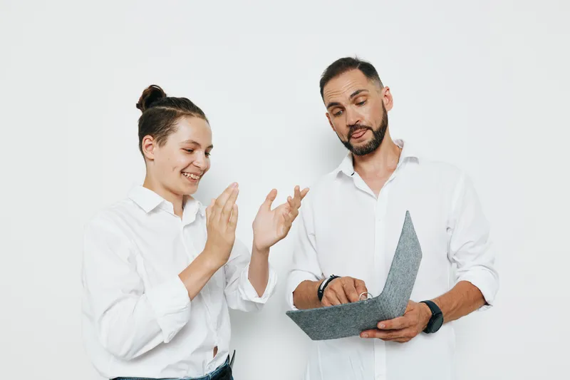 A professional man on an isolated colored background, presenting a confident business demeanor, focused mood, and calm emotion as he reviews a document with a colleague.