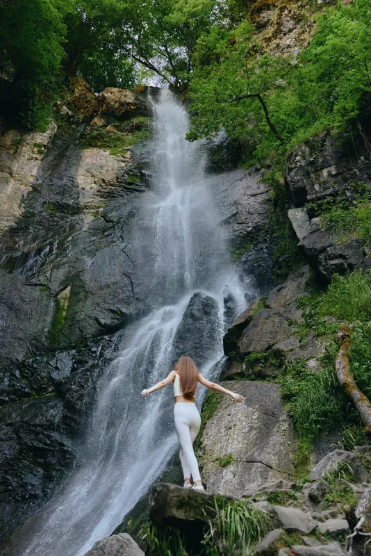 woman standing near waterfall in lush green forest, natural scenery, flowing water, outdoor adventure, casual clothing