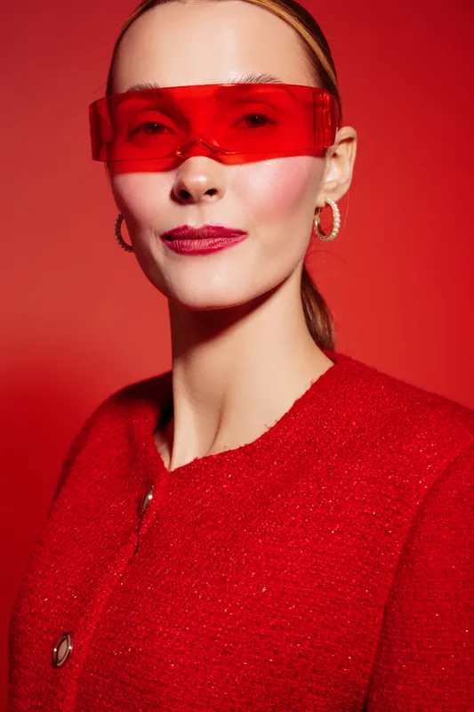 Portrait of confident woman wearing red sunglasses and red jacket on red background. Fashion concept with bold colors and modern style in studio lighting.
