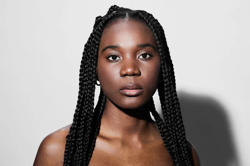 Portrait of a confident young Black woman with braided hair against a minimalistic background, radiating empowerment and self assurance