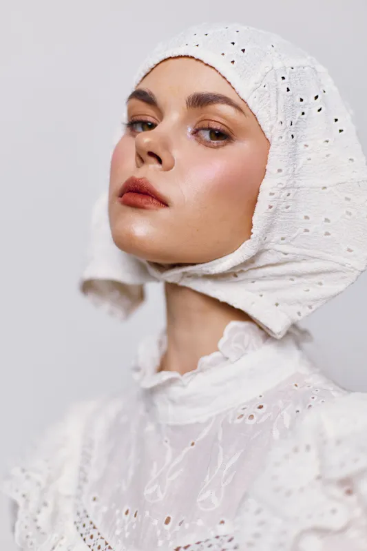 Young woman in a white lace dress and headscarf, showcasing confidence and elegance against a neutral backdrop, ideal for fashion or cultural themes