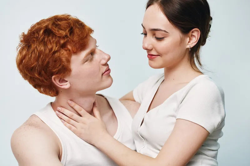 Couple, love, intimacy and connection with young man and woman looking at each other in white background. Relationship, affection and close moment with casual clothing and gentle touch.
