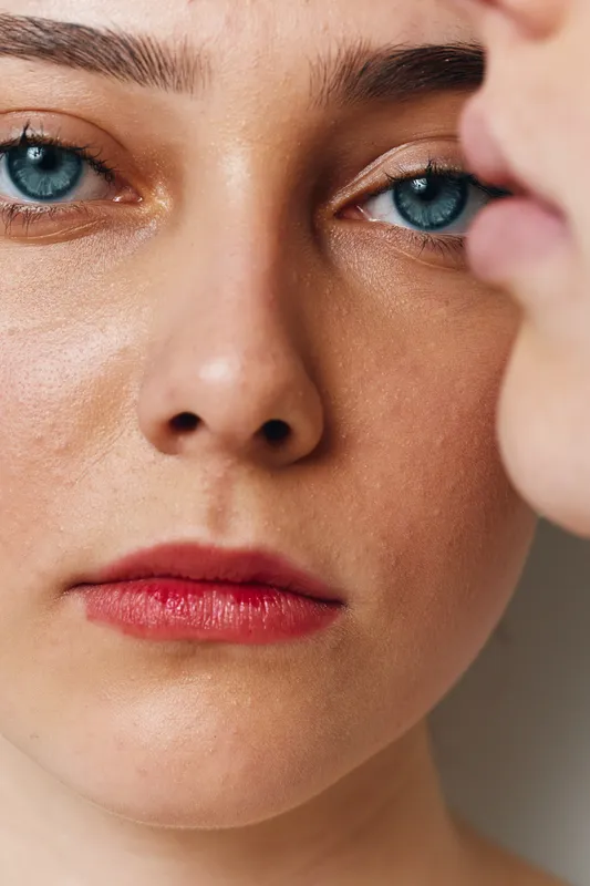 Woman with blue eyes and red lips in closeup portrait showing natural skin texture and detailed facial features with soft light and shallow depth of field.