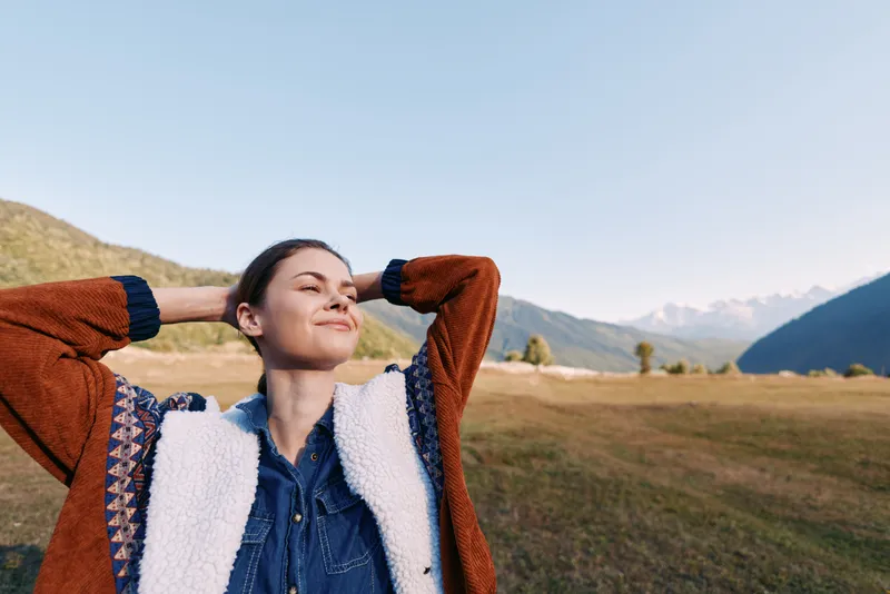 Woman in nature, mountains and meadow, relaxed with eyes closed and smiling. Portrait of happiness, outdoor lifestyle and peaceful moment enjoying fresh air and scenic landscape.
