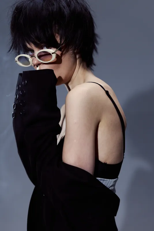 Stylish woman with short black hair wearing sunglasses and black jacket in moody lighting