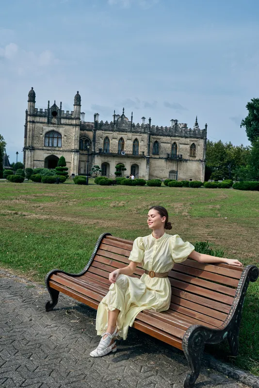 woman on bench in park with historic building background wearing vintage dress, relaxed pose authenticity inclusivity light