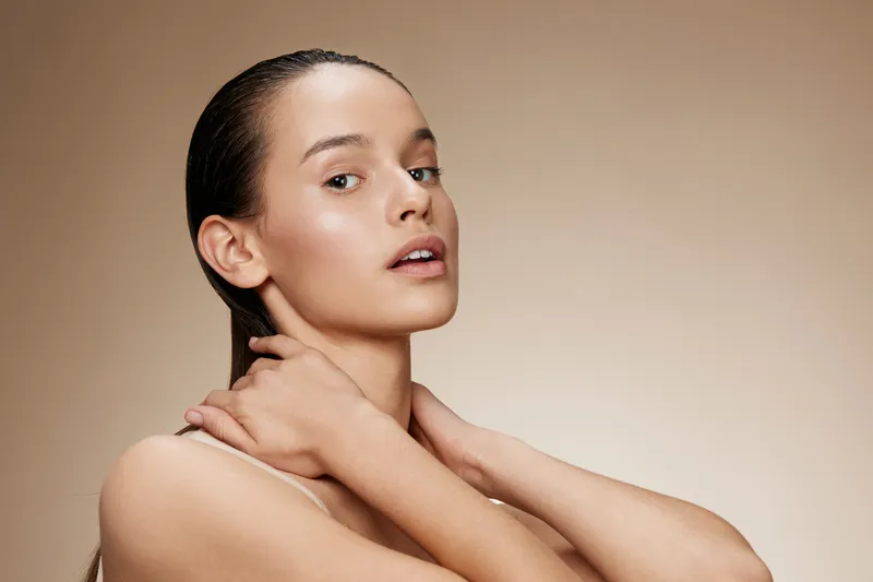 Elegant young woman with long hair showcasing natural beauty against a soft beige background, promoting skincare and healthy living