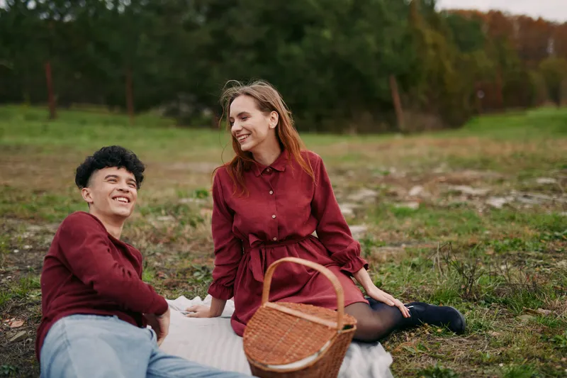 A young couple enjoys a genuine picnic on a grassy field, relaxed and naturally smiling, conveying authenticity and believable connection in simple everyday moments together.