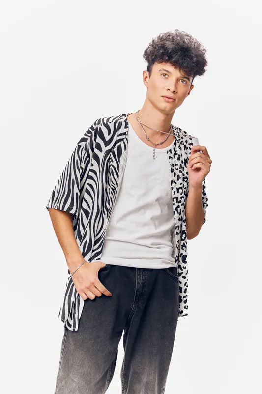 young man in stylish black and white patterned shirt and white t-shirt posing with relaxed expression against a white background, casual fashion look, curly hair