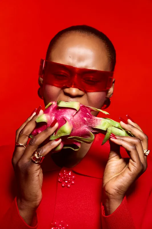 Close-up of dark skinned African woman biting a dragon fruit. The vibrant red background and red outfit create a bold contrast. Concept of healthy eating, fruit, and culture.