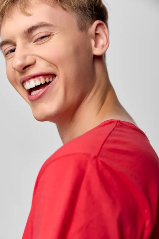 Joyful young man wearing a red shirt, captured in a close up moment of happiness and laughter, conveying friendly energy and warm mood for lifestyle and marketing visuals.