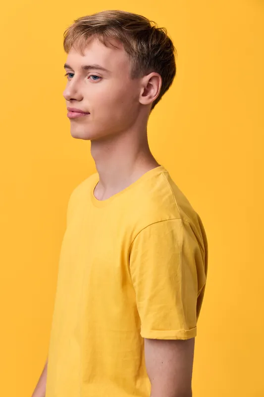 Yellow shirt with side profile in studio lighting for fashion and color study, monochrome background, casual wear, clean lines, minimal composition, youthful style, confident pose, lighting enhances
