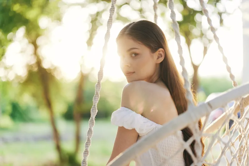 Young woman in white dress enjoying sunny day on hammock, showcasing natural beauty and serene emotions among green trees Perfect for lifestyle and wellness themes