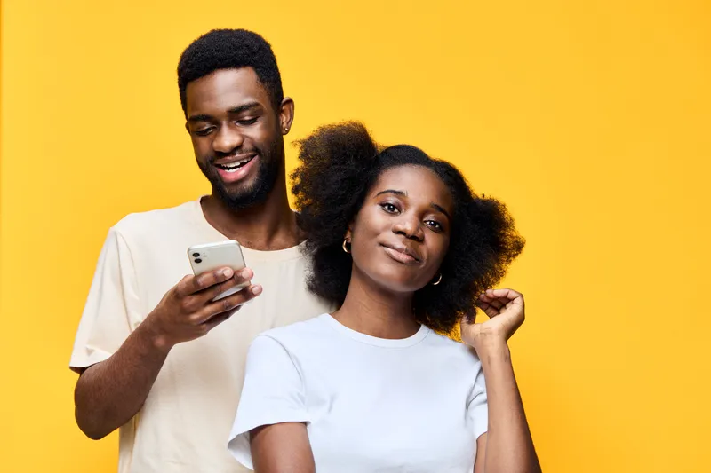 A joyful young couple posing together on a bright yellow background, showcasing modern casual attire and playful emotions, perfect for lifestyle themes