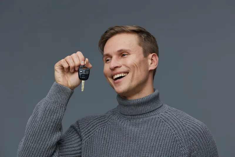 smiling young man holding car key casual grey turtleneck sweater happy emotions studio portrait cybersecurity concept