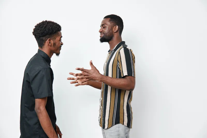 Two african american men with dark skin talking and gesturing in casual clothes against white background in studio. Communication, friendship and discussion concept.