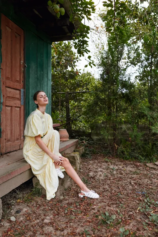 Portrait of a woman sitting on steps beside a doorway in a garden outdoors in calm light presenting a relaxed fashion vibe and natural beauty and serene mood