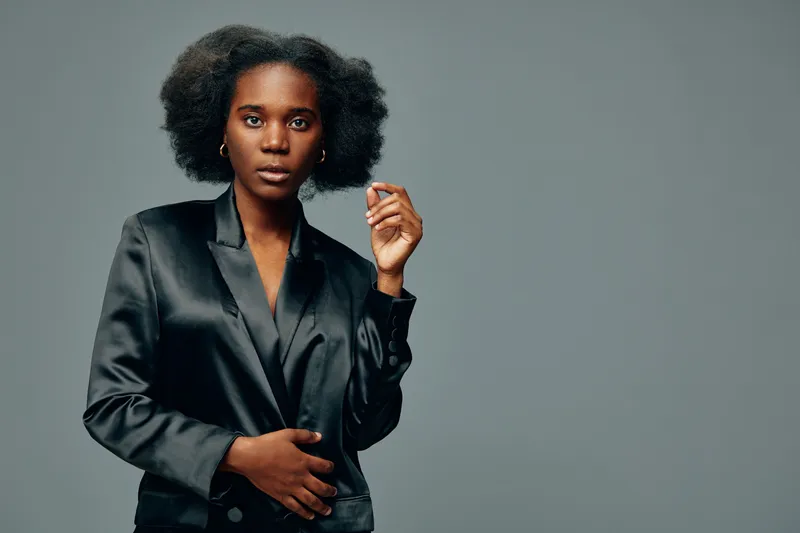 Confident Black woman in elegant black blazer with natural hair, conveying strength and determination against a minimalist grey background