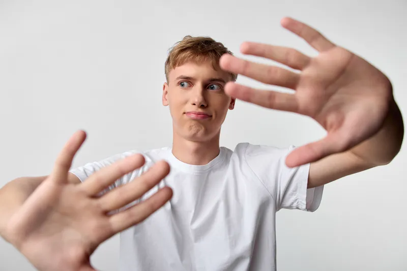 Hands reach toward the camera as a focused man raises arms in a framed barrier like pose, creating tension and expression in a studio setting