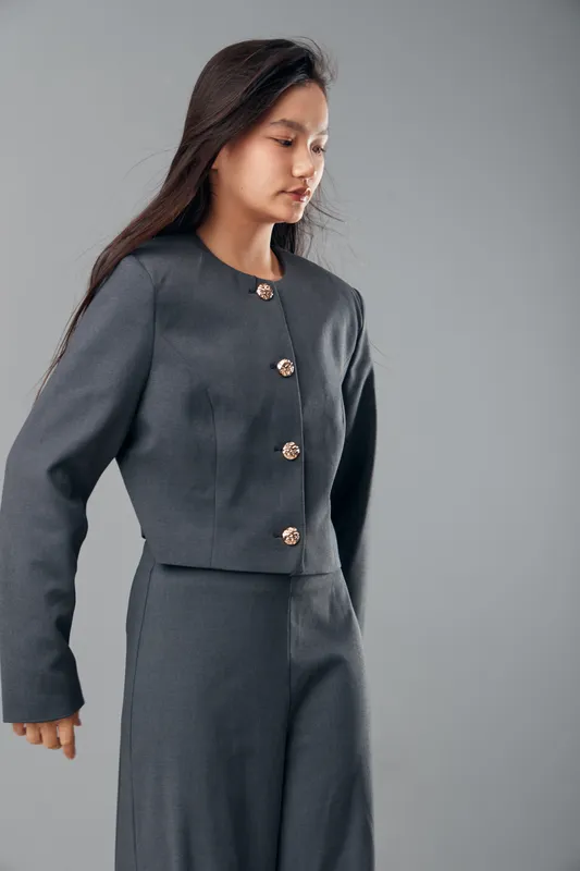 Woman in elegant dark gray formal suit with decorative buttons posing on plain background. Business fashion, style, confidence, and professionalism for office or job setting.