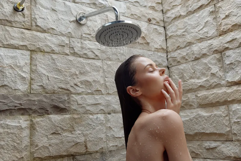 woman taking shower with water droplets on skin, natural stone background, relaxation, calm and peaceful moment under rainfall showerhead indoors