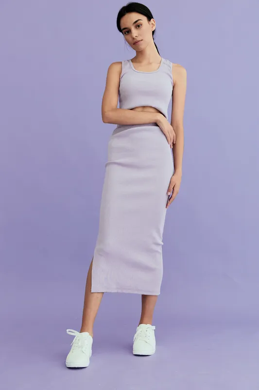 Young woman wearing casual lavender ribbed dress and white sneakers standing against pastel purple background with minimalistic and modern style.