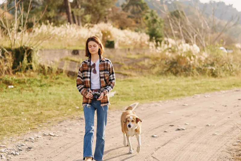 Woman, dog, walking, outdoors, park, casual apparel and relaxed stride along a sunlit dirt path, enjoying fresh air, nature, and a peaceful moment together.
