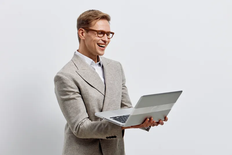 happy young caucasian man holding laptop wearing glasses check digital nomad work remote business concept on light background