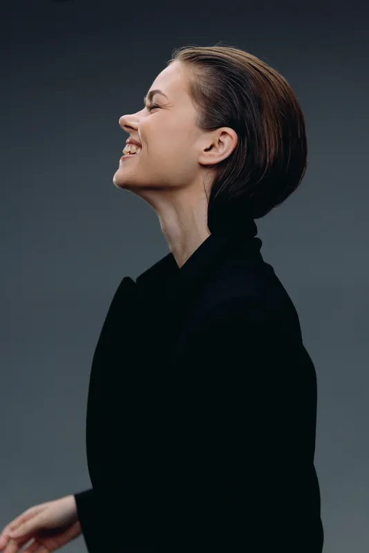 Smiling woman in black coat with short hair against dark background expressing joy and confidence.