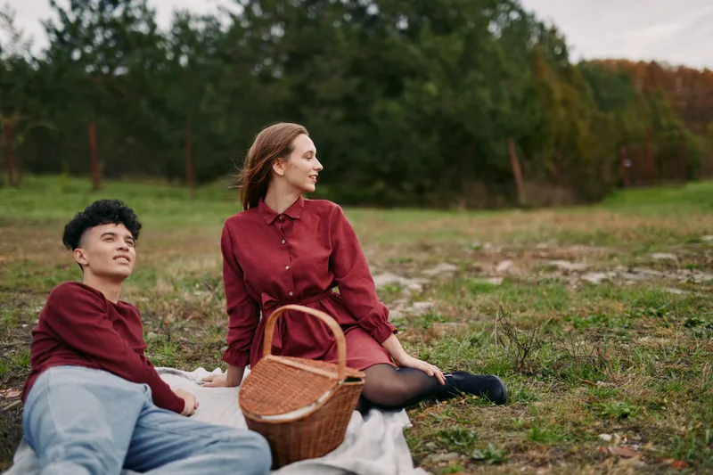 A genuine, authentic candid portrait of a couple sharing a relaxed picnic outdoors on a blanket, capturing natural expressions, quiet connection and real life moments in soft autumn light.