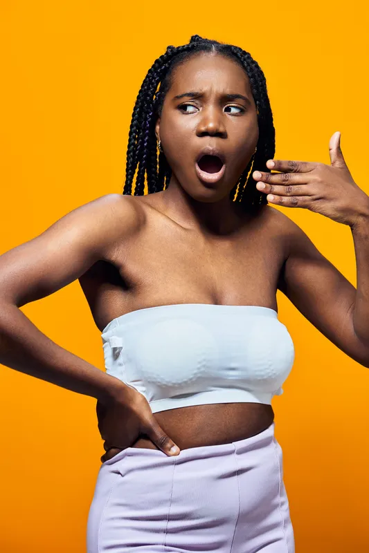 Surprised Black woman in a strapless top expressing shock, with a vibrant yellow background, capturing emotions and modern style