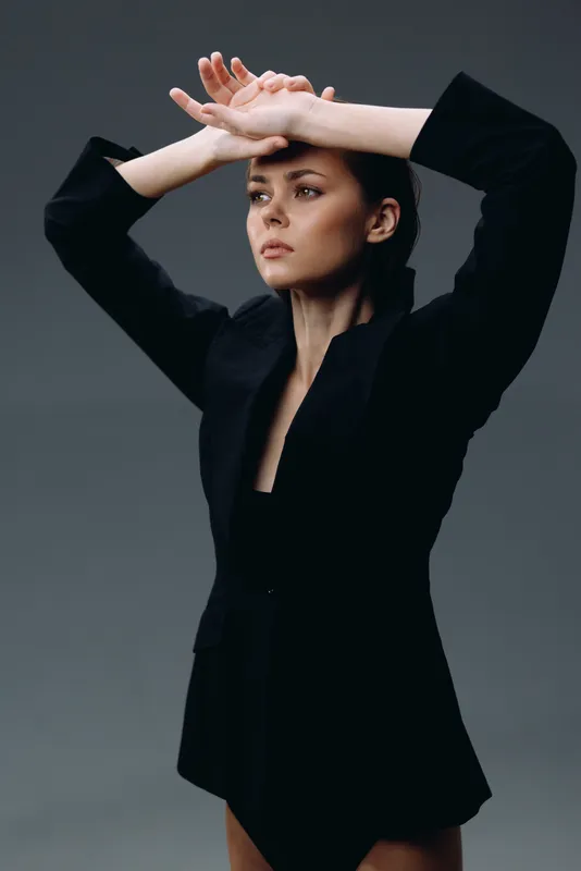 Serious woman in black blazer posing thoughtfully against dark background with dramatic lighting and minimal style