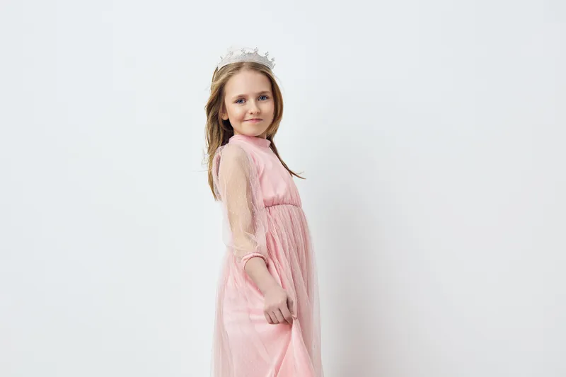 Young girl in a pink dress with a crown, showcasing confidence and joy against a light background, ideal for children s fashion and celebrations