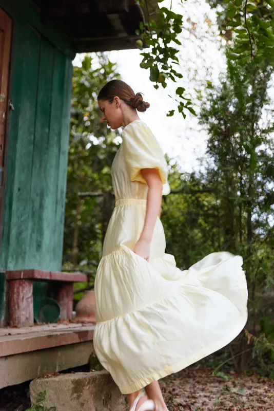 Woman in flowing yellow dress stepping up cottage porch in nature, motion and summer outdoor scene, authenticity inclusive serene
