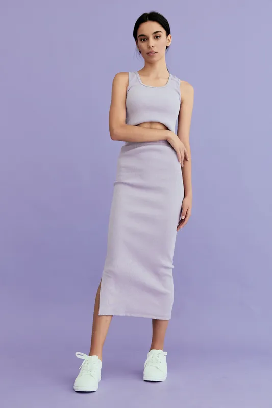 woman in casual lilac dress stands confidently on purple background wearing white sneakers, showing relaxed and modern style for everyday wear inspiration.