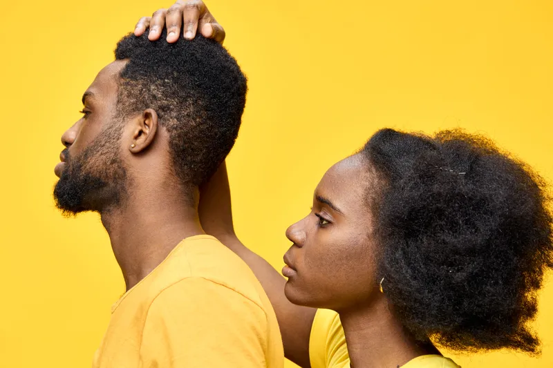 A portrait of an African couple with natural hairstyles against a vibrant yellow background, showcasing intimacy and connection through their emotions and attire