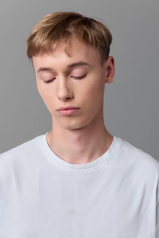 Young man, closed eyes, serenity, white tshirt, calm demeanor in a neutral studio, soft lighting emphasizes tranquility and focus in a minimal composition