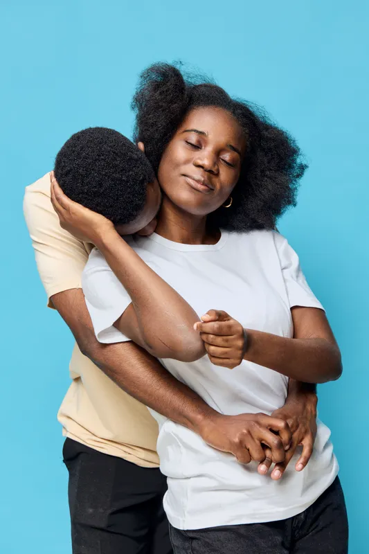 A joyful couple embracing each other against a vibrant blue background, showcasing love and connection while wearing casual outfits