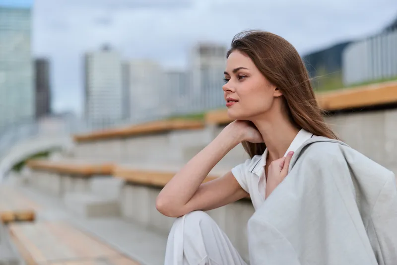 Confident woman in business attire sitting outdoors, showcasing professionalism and poise in a modern urban environment.