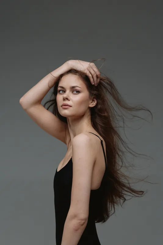 young woman in black dress posing with flowing hair on gray background, elegant, natural, beauty