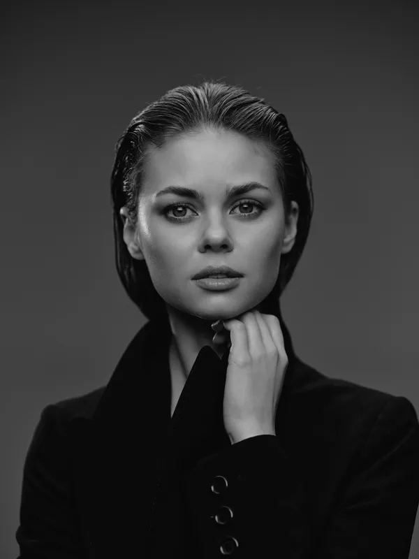 Black and white portrait of a serious woman with wet hair wearing a dark coat in a studio setting