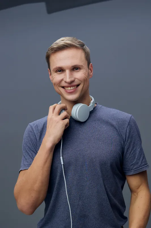 Smiling man with headphones wearing casual t-shirt on plain gray background studio portrait. People lifestyle concept, relaxed, cheerful, positive, youthful, modern, entertainment, music, happiness.